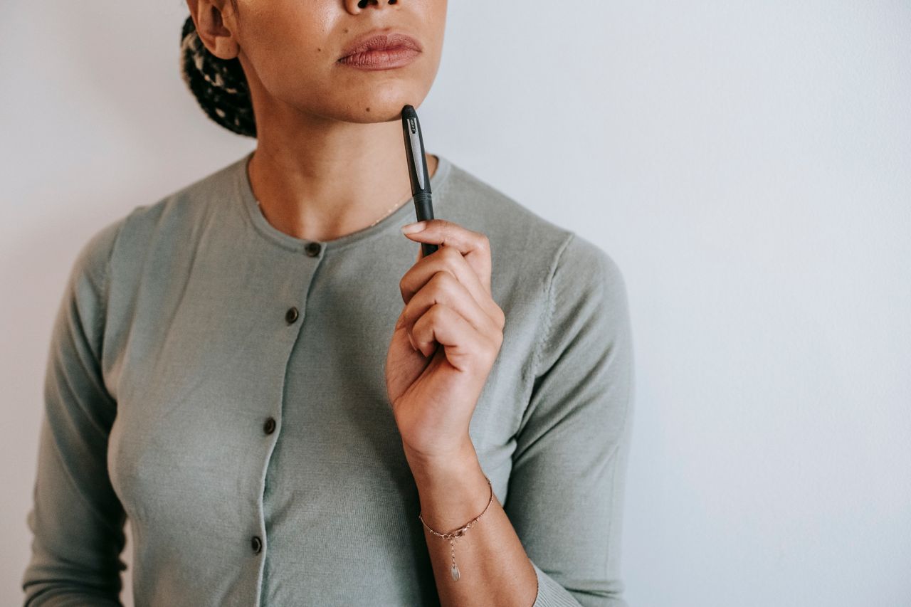 Person standing resting a pen on their chin